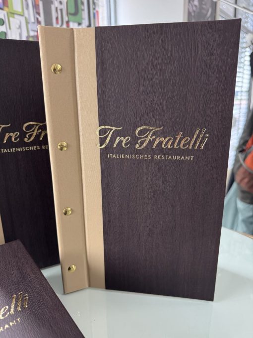 Zweifarbige Speisekartenmappen im Querformat für das Ristorante Tre Fratelli in Beige und Holzoptik mit Goldschrauben