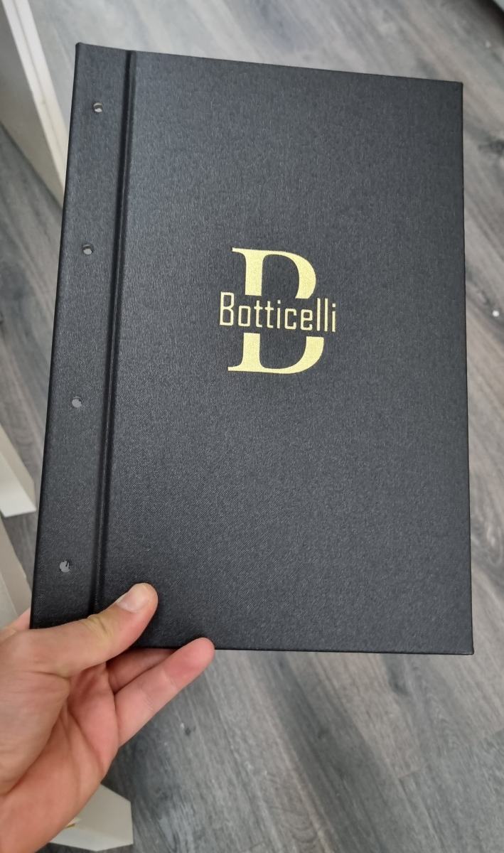 Schwarze Speisekartenmappe des Restaurants Botticelli mit goldenem Logo, in der Hand gehalten