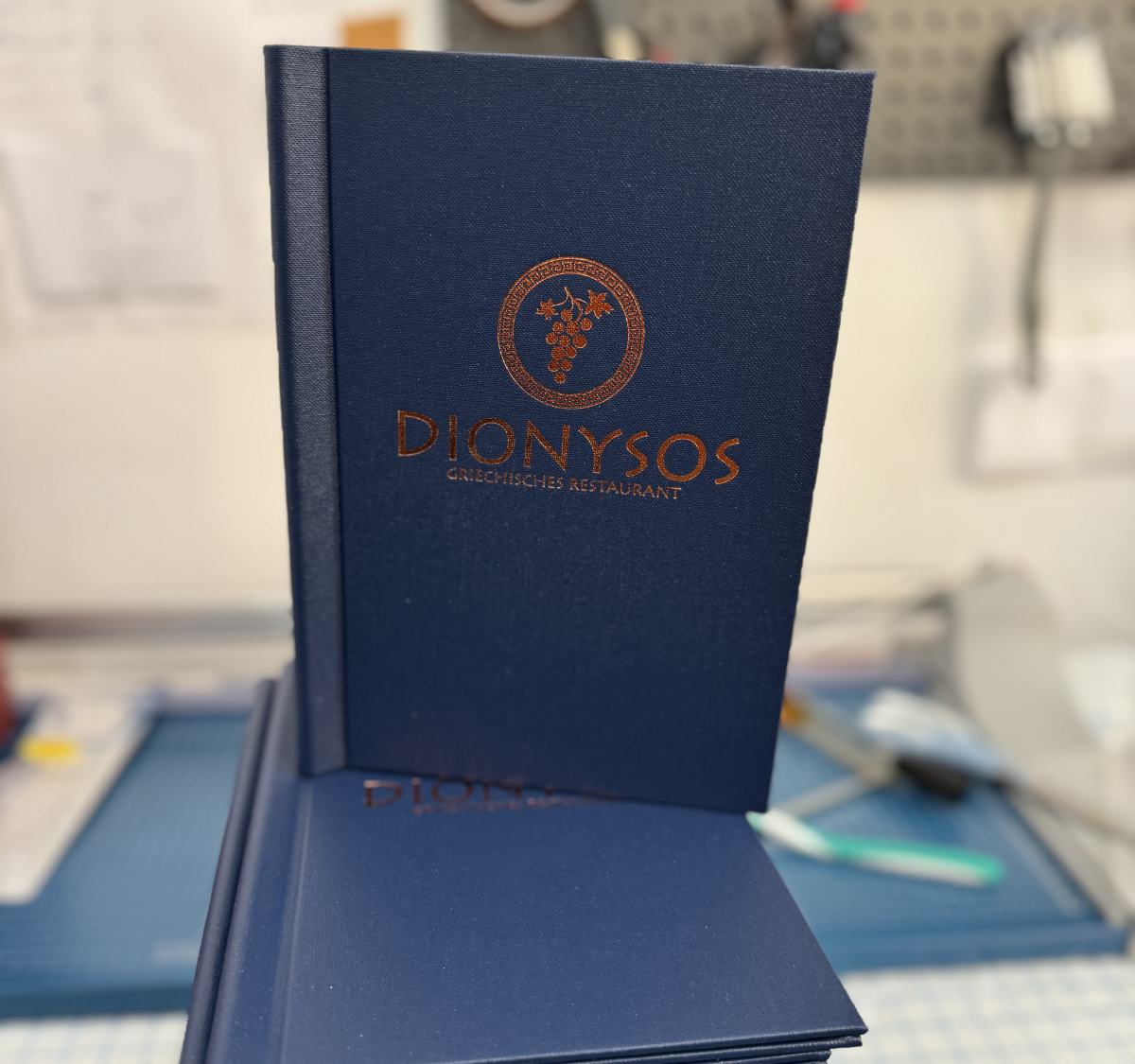 Dunkelblaue Speisekartenmappe des griechischen Restaurants Dionysos mit Logo in Kupferprägung
