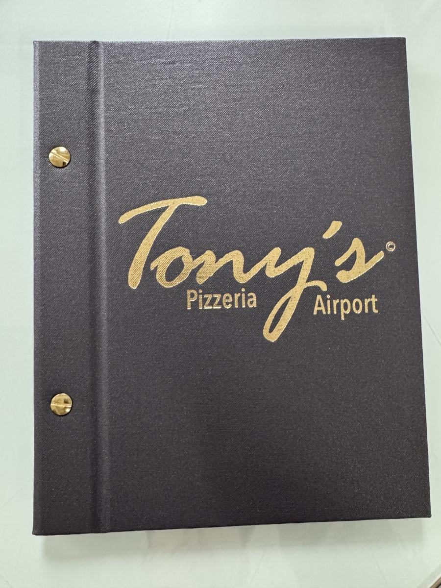 Graue Speisekartenmappe der Pizzeria Tony’s Airport mit goldener Logoprägung und Messingschrauben