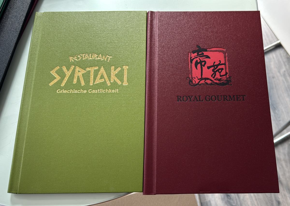 Zwei Klemmspeisekarten nebeneinander: Restaurant Syrtaki in Grün mit Goldprägung und Royal Gourmet in Bordeaux