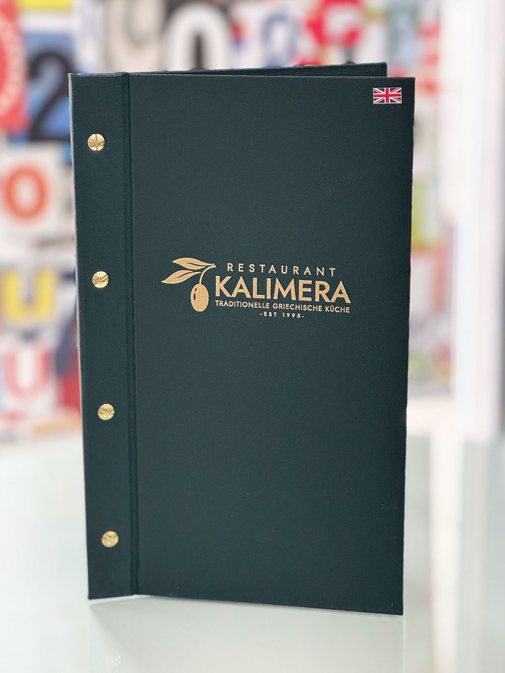 Dunkelgrüne Speisekarte des Restaurants Kalimera mit Goldprägung und Sprachkennzeichnung