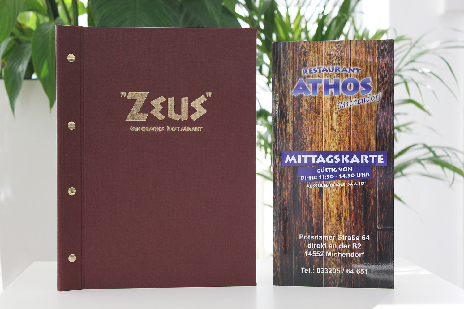 Bordeauxrote Speisekarte des Restaurants Zeus neben einer gedruckten Mittagskarte